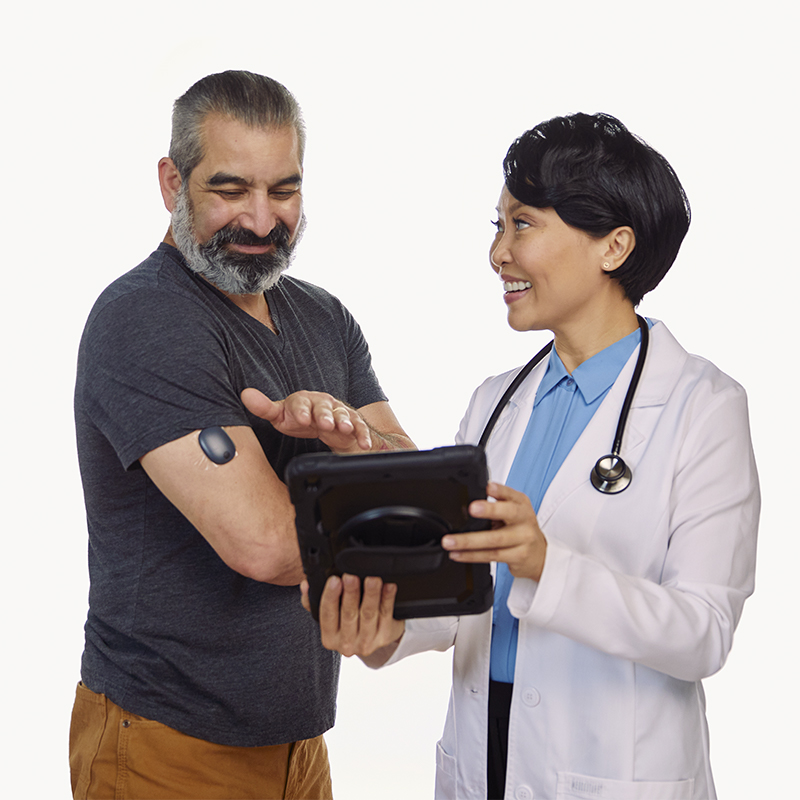 A healthcare provider shows a patient how to track glucose data from an implanable cgm on a tablet.