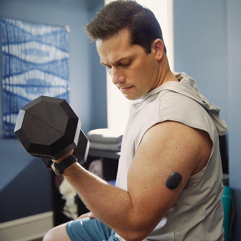 Man lifting weights at the gym while using a CGM system on his arm.